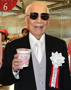 Hombre con gafas de sol y traje posa con paquete de comida.