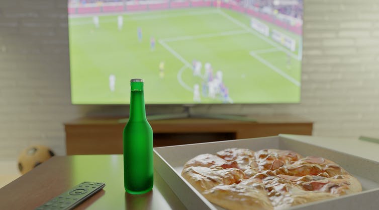 Botella de cerveza y pizza en la mesa frente al televisor que muestra el partido de fútbol.