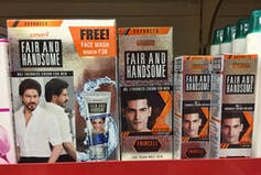 Productos para aclarar la piel en un estante, con imágenes de hombres asiáticos y el nombre 'Fair And Handsome'.