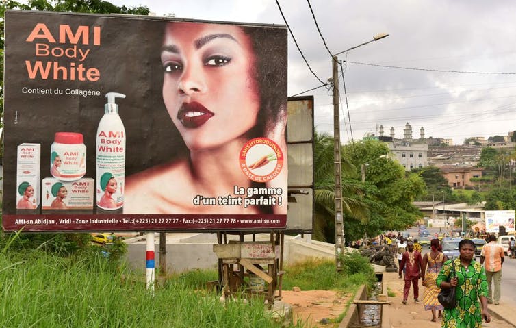La gente pasa frente a una valla publicitaria con una mujer de aspecto glamoroso, junto con las palabras